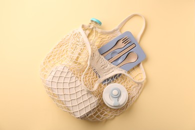 Photo of Fishnet bag with different items on beige background, top view. Conscious consumption
