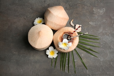Photo of Young peeled coconuts with straw, palm leaf and beautiful flowers on grey table, flat lay