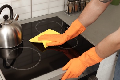 Photo of Young man cleaning oven cooktop with rag in kitchen, closeup