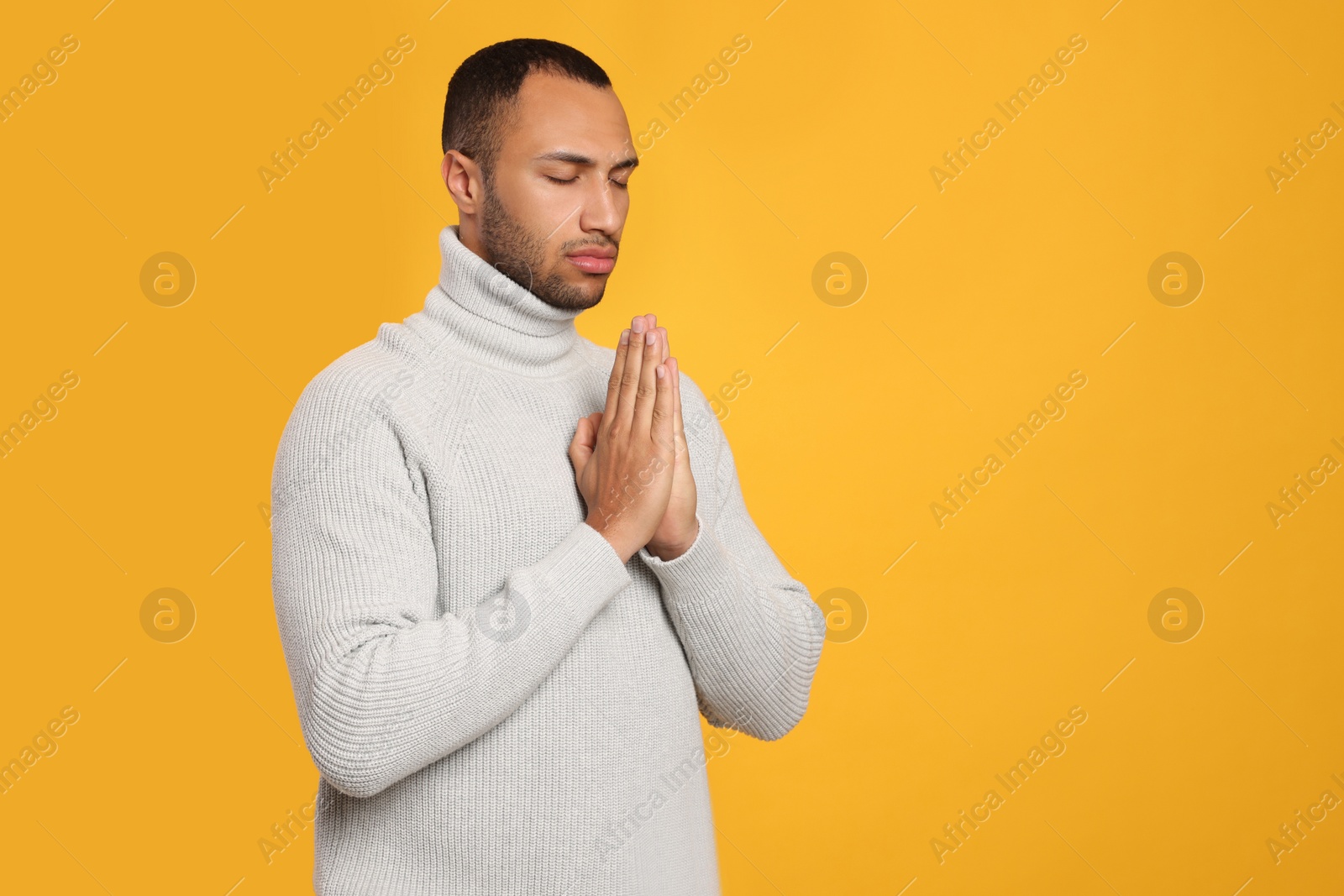 Photo of African American man with clasped hands praying to God on orange background. Space for text