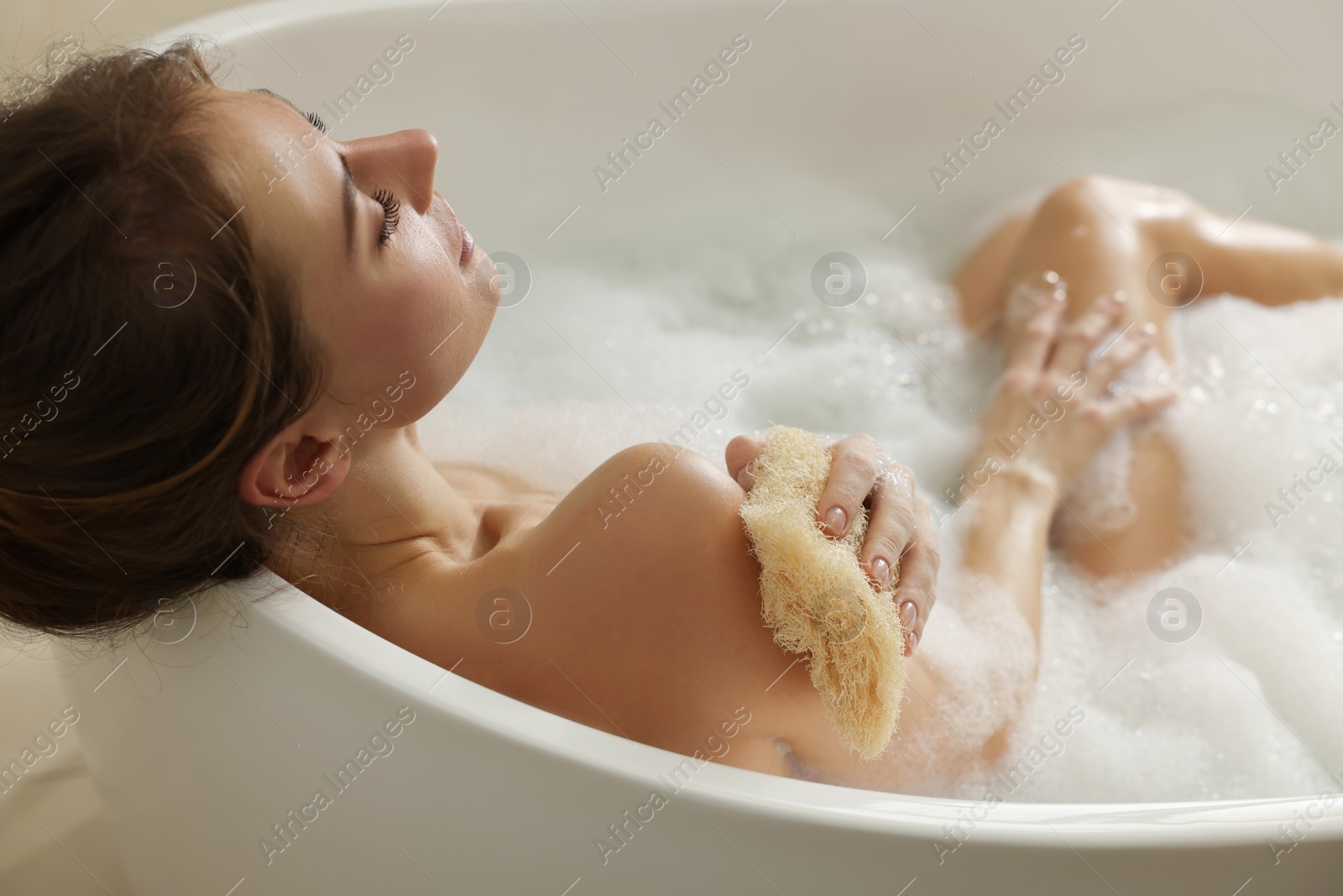 Photo of Beautiful woman with loofah taking bath indoors