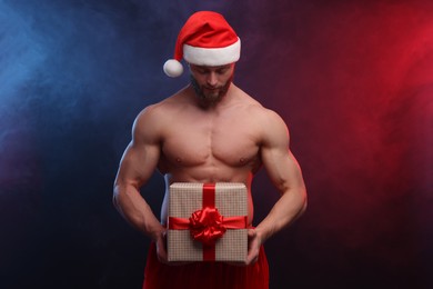 Photo of Attractive young man with muscular body holding Christmas gift box on color background