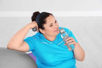 Tired overweight woman drinking water in gym