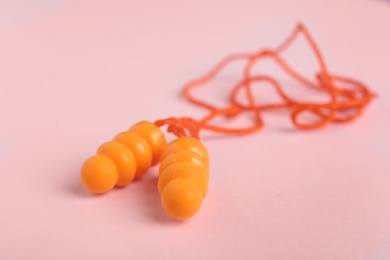 Photo of Pair of orange ear plugs with cord on pink background, closeup