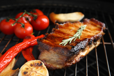 Photo of Delicious ribs with rosemary and vegetables on barbecue grill