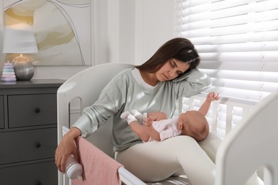Photo of Tired young mother sleeping in crib with her baby at home