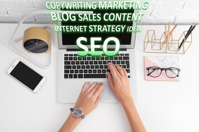 Image of Search engine optimization (SEO). Copywriter working on laptop at white table, top view. Many words coming out of computer