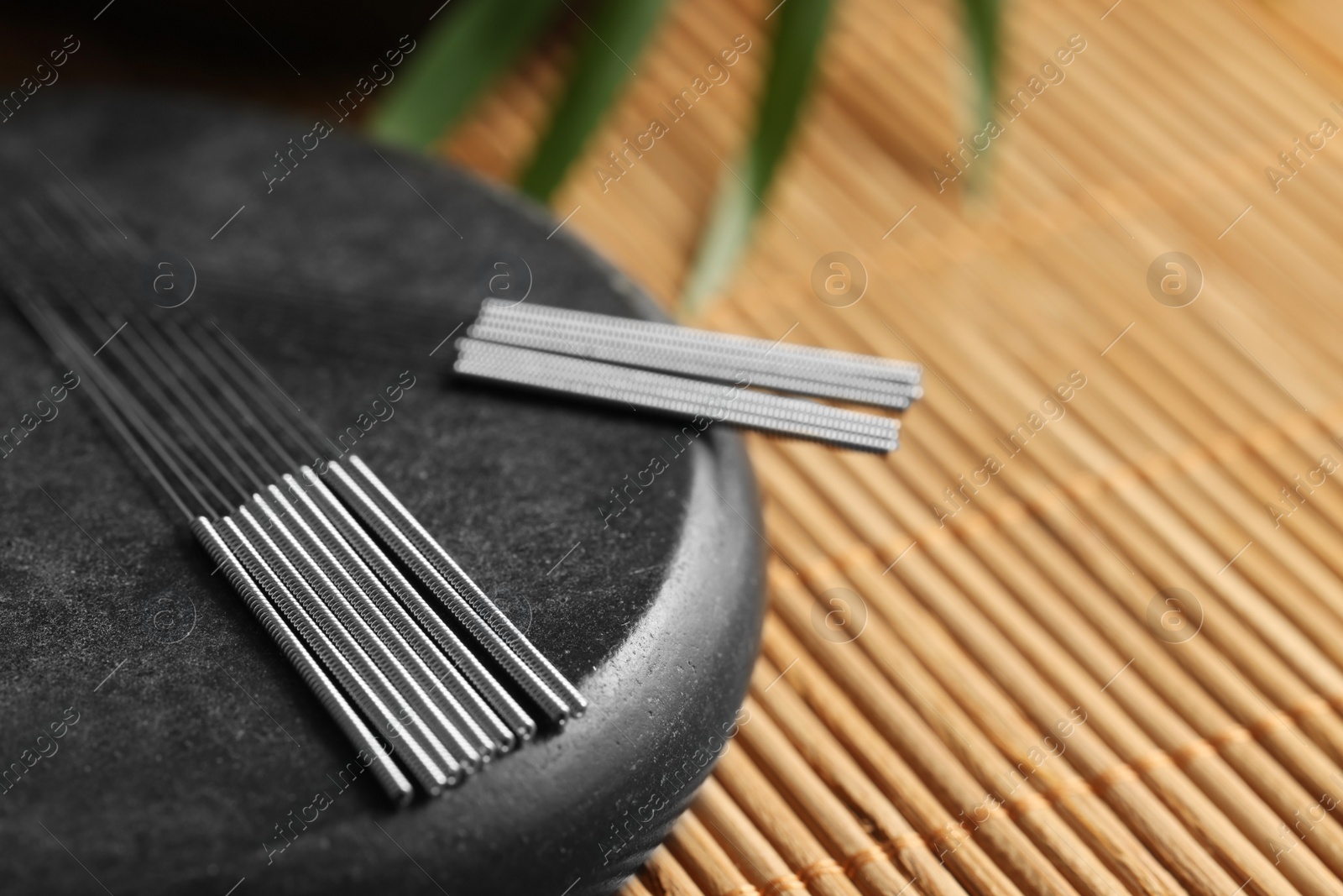 Photo of Acupuncture needles and spa stone on bamboo mat, closeup. Space for text