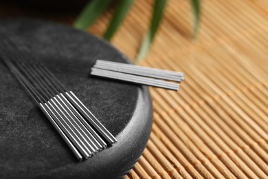 Photo of Acupuncture needles and spa stone on bamboo mat, closeup. Space for text