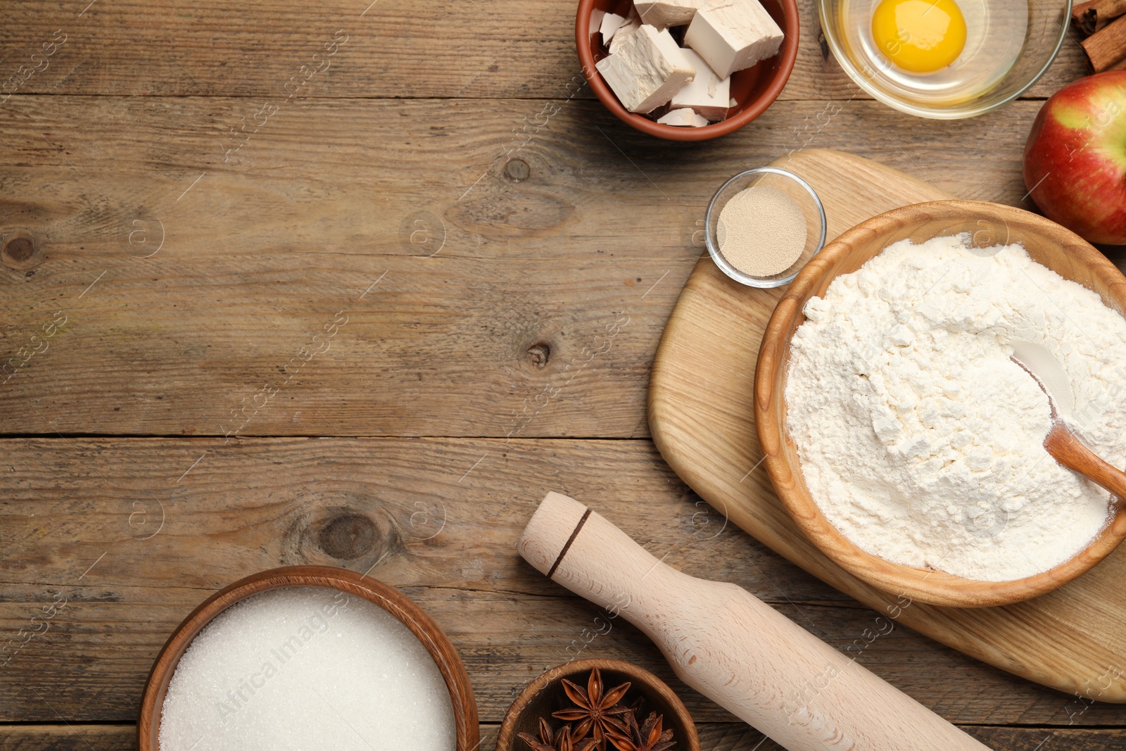 Photo of Flat lay composition with flour, rolling pin and ingredients on wooden table, space for text. Cooking yeast cake