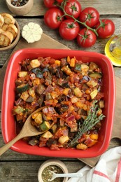 Photo of Dish with tasty ratatouille, ingredients and bread on wooden table, flat lay