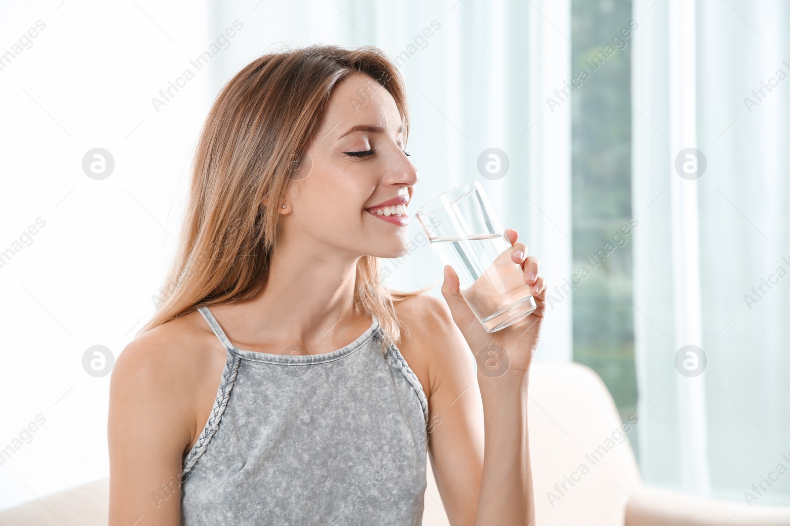 Photo of Young woman drinking clean water from glass at home