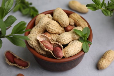 Photo of Fresh unpeeled peanuts in bowl and green leaves on grey table, closeup