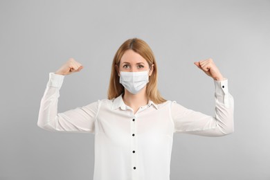 Photo of Woman with protective mask showing muscles on light grey background. Strong immunity concept