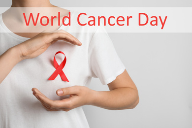 Image of Woman with red ribbon on t-shirt against light background. World Cancer Day