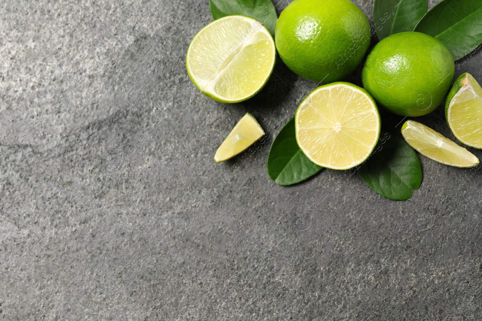 Photo of Fresh ripe limes and leaves on grey table, top view. Space for text