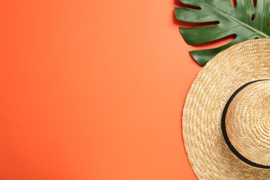 Stylish straw hat and tropical leaf on orange background, flat lay. Space for text