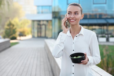 Smiling businesswoman talking on smartphone during lunch outdoors. Space for text