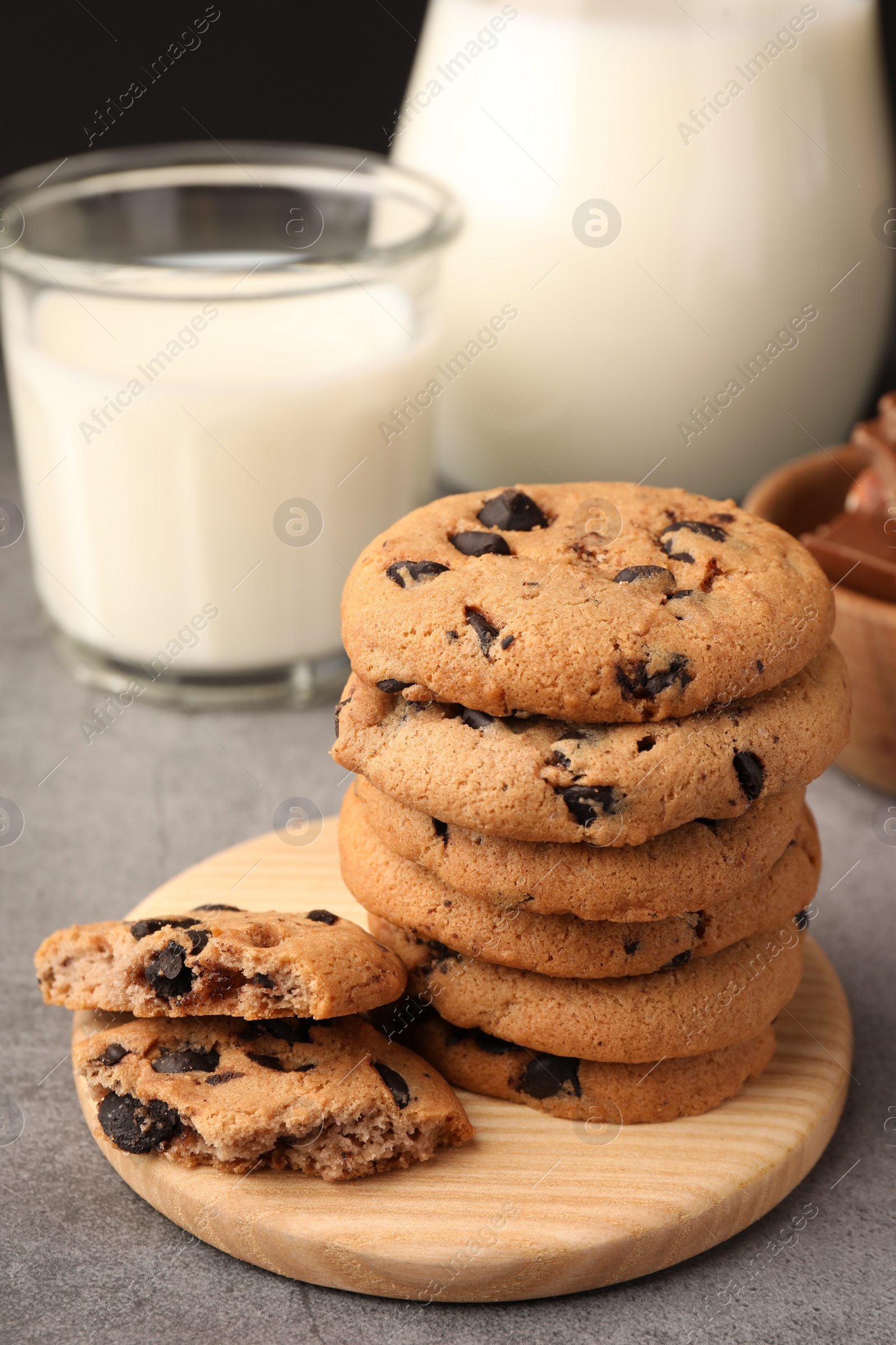 Photo of Stack of delicious chocolate chip cookies and milk on grey table