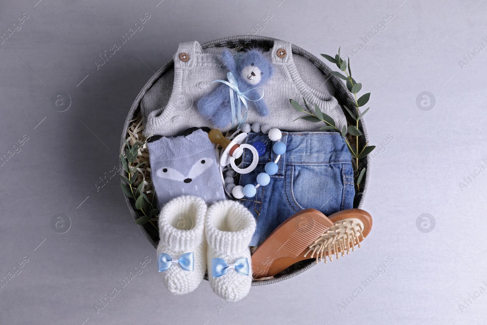 Photo of Box with baby clothes, booties and accessories on grey background, top view
