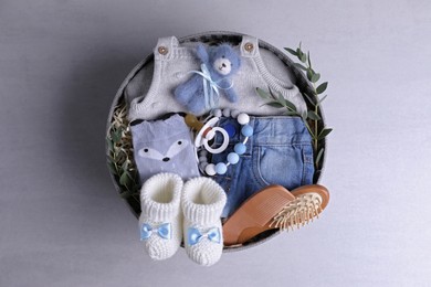Photo of Box with baby clothes, booties and accessories on grey background, top view