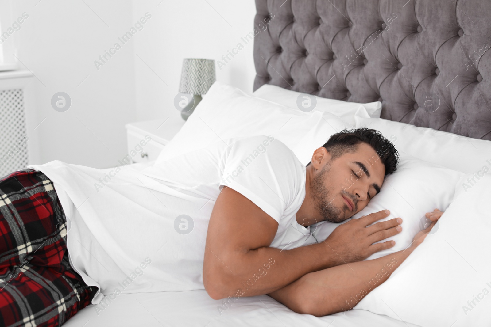 Photo of Young man sleeping on bed with soft pillows at home