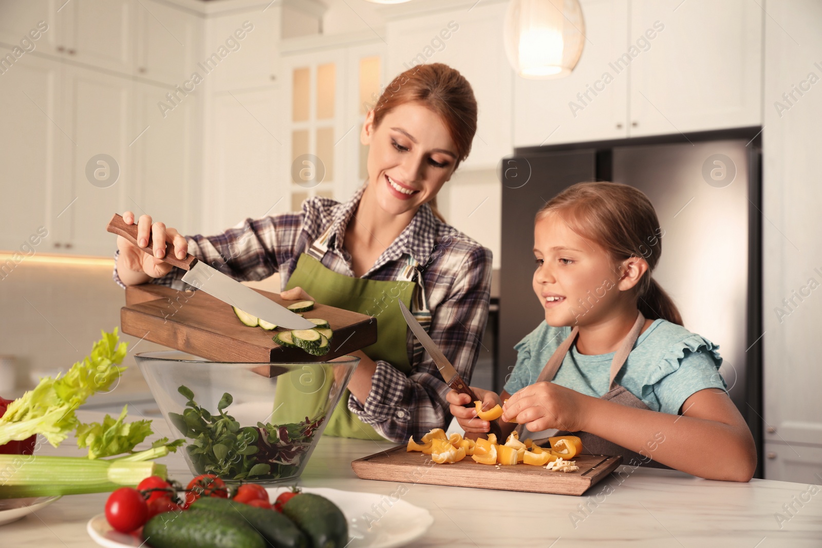 Photo of Mother and daughter cooking salad together in kitchen