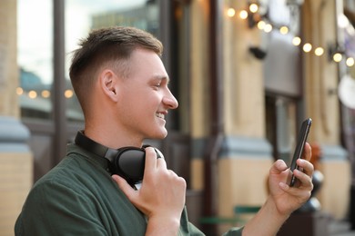 Photo of Smiling man with headphones using smartphone outdoors