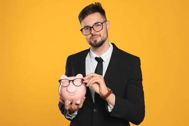 Handsome businessman with piggy bank on orange background