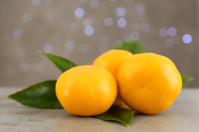 Photo of Tangerines with green leaves on grey table against blurred lights