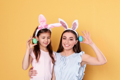 Photo of Mother and daughter in bunny ears headbands with Easter eggs on color background