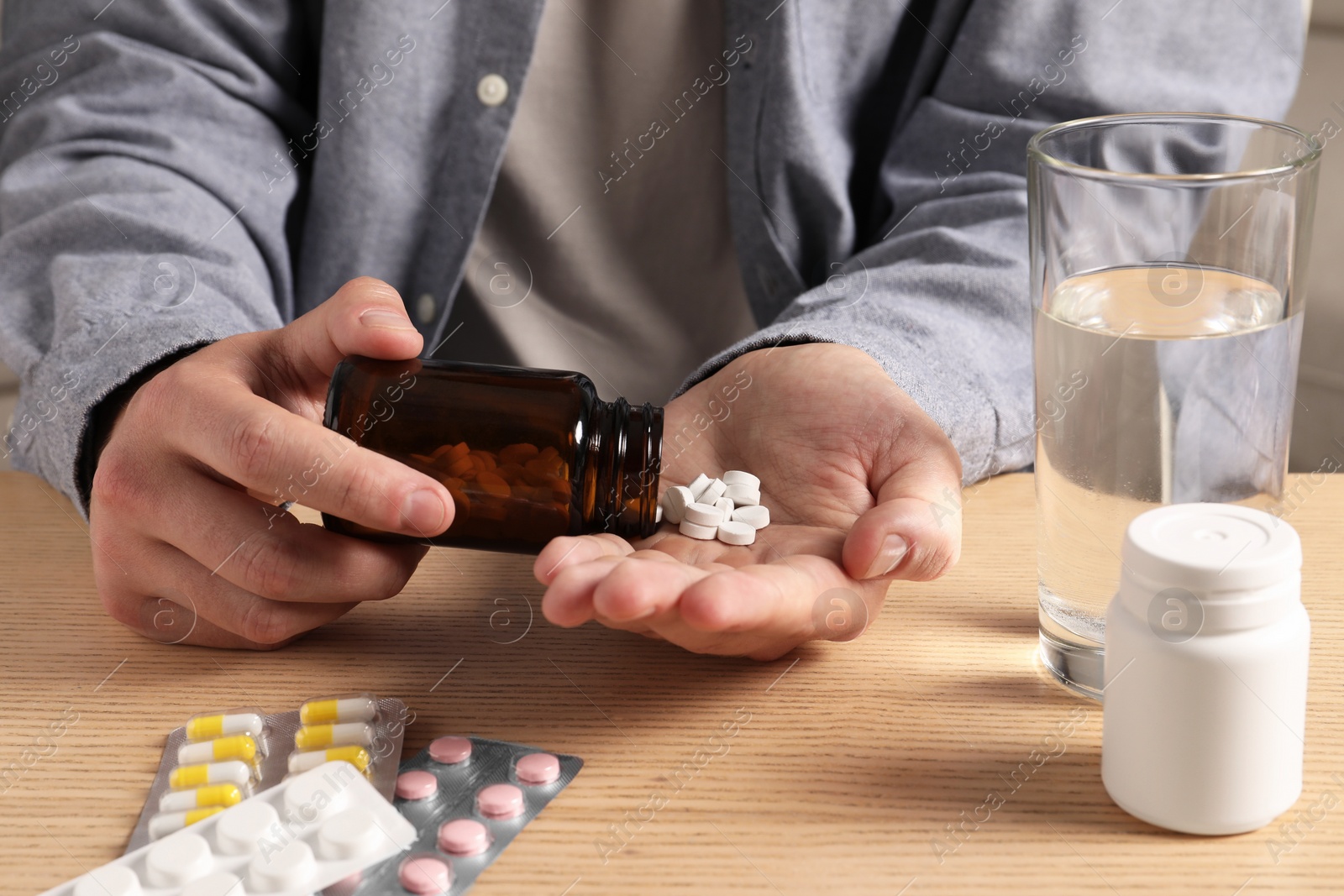 Photo of Man pouring pills from bottle at wooden table, closeup