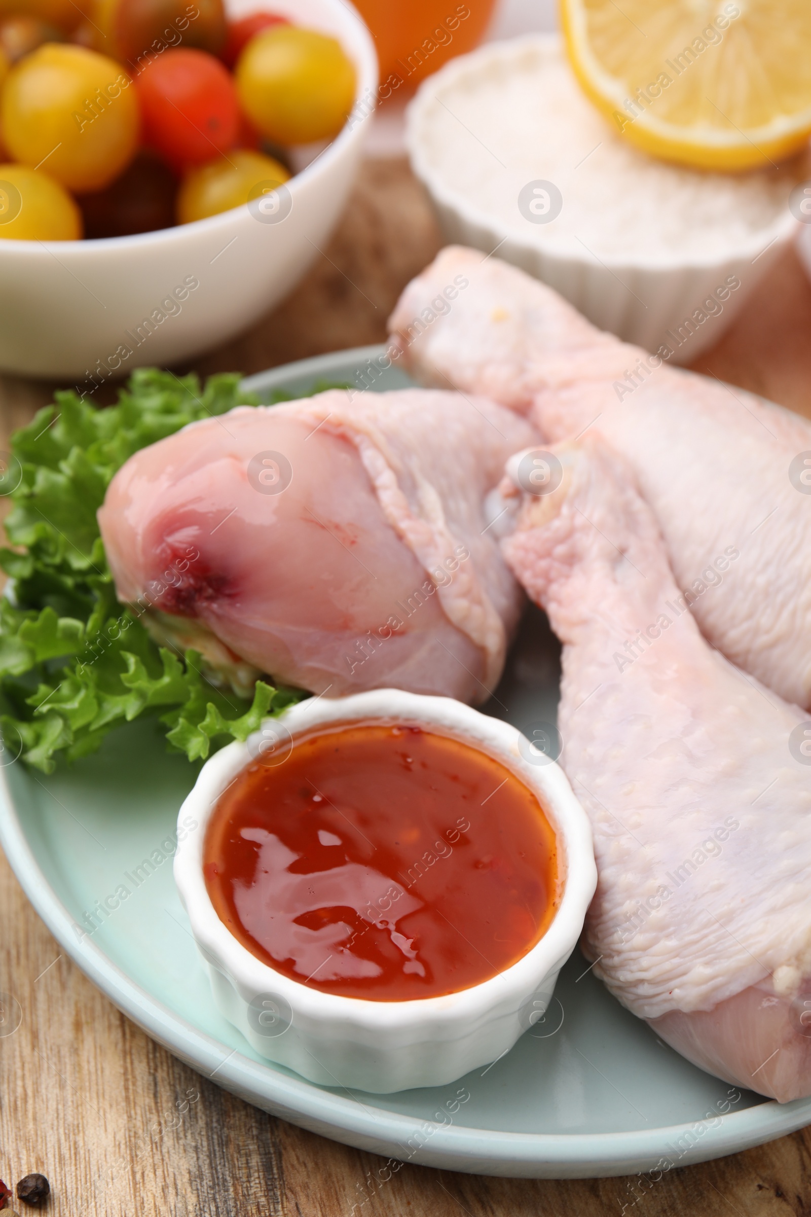 Photo of Fresh marinade, raw chicken drumsticks and lettuce on wooden table, closeup