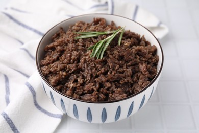 Photo of Fried ground meat in bowl and rosemary on white tiled table, closeup