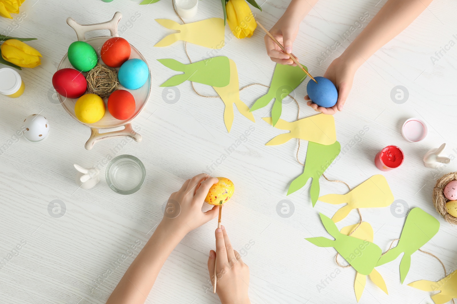 Photo of Little children painting Easter eggs at white wooden table, top view