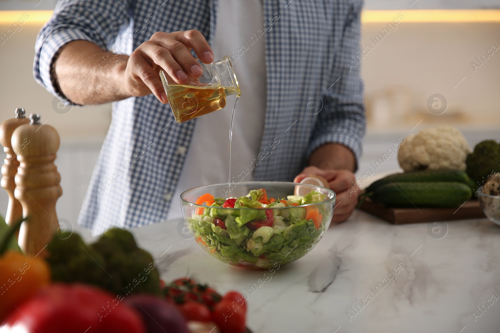 Photo of Man cooking salad at table in kitchen, closeup