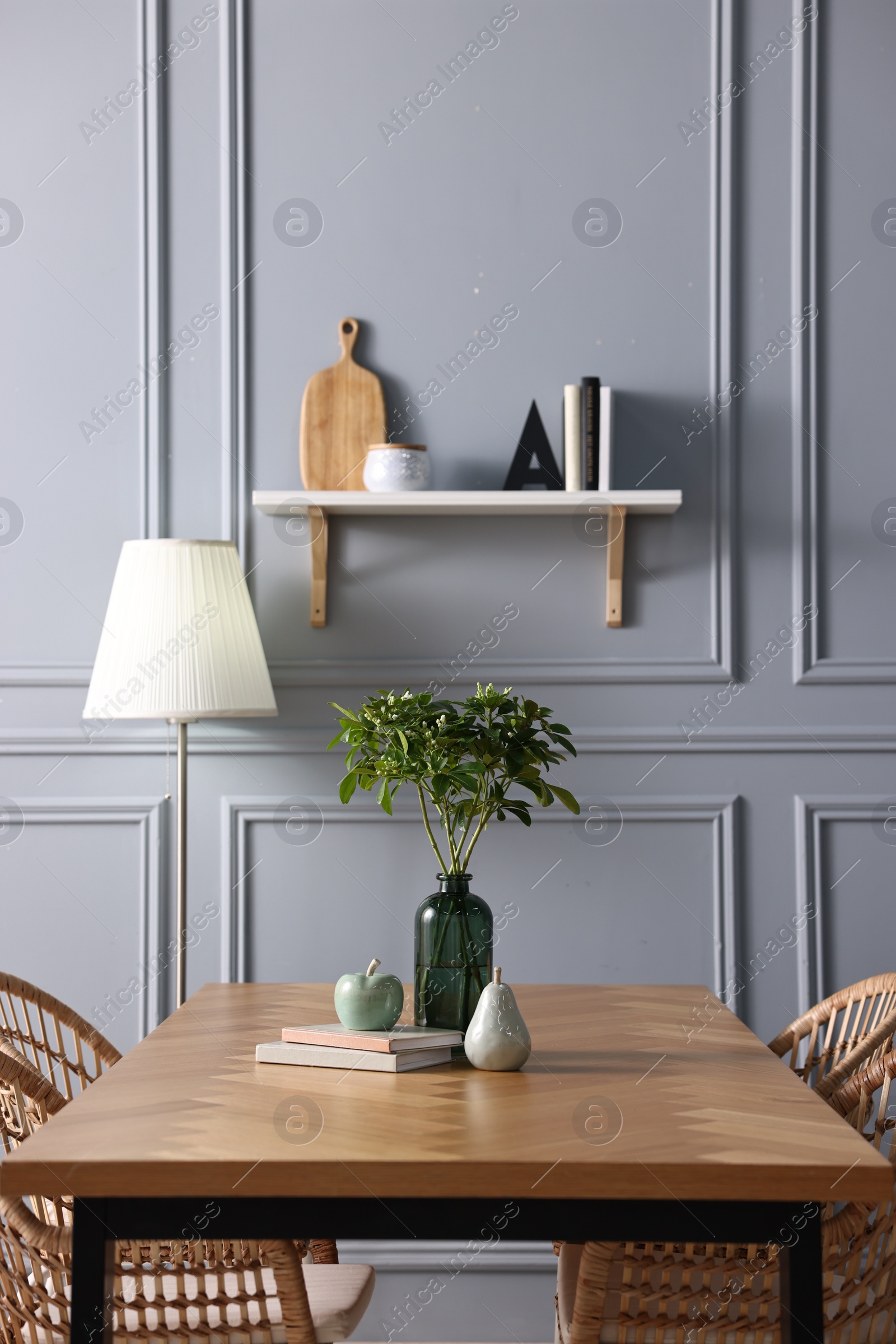 Photo of Vase with green branches, books and decor on wooden table in stylish dining room