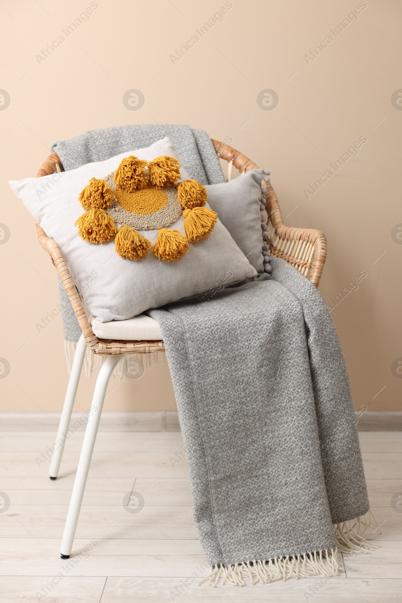 Photo of Stylish soft pillow and blanket on armchair near beige wall indoors