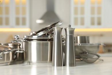 Photo of Set of shiny cooking utensils on white table against blurred background