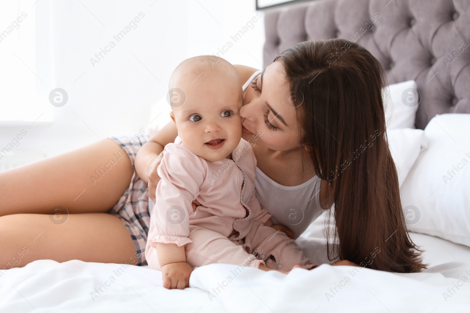 Photo of Young mother with her cute baby girl on bed at home