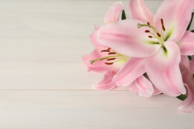 Photo of Beautiful pink lily flowers on white wooden table, closeup. Space for text