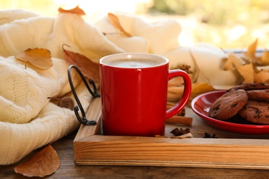 Composition with cup of hot drink, sweater and autumn leaves on windowsill. Cozy atmosphere