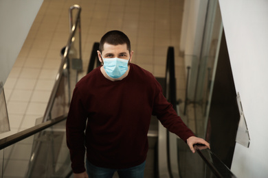 Photo of Man with disposable mask on escalator in mall. Dangerous virus