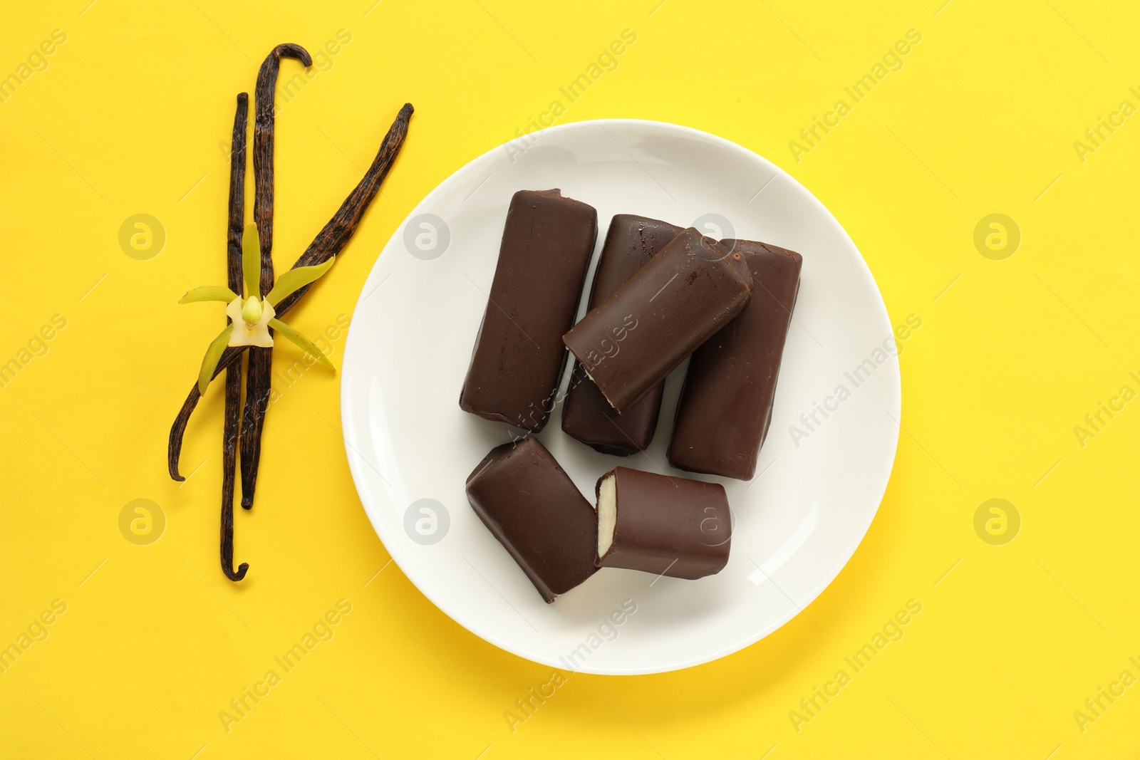 Photo of Glazed curd cheese bars, vanilla pods and flower on yellow background, top view