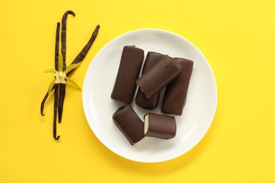 Glazed curd cheese bars, vanilla pods and flower on yellow background, top view