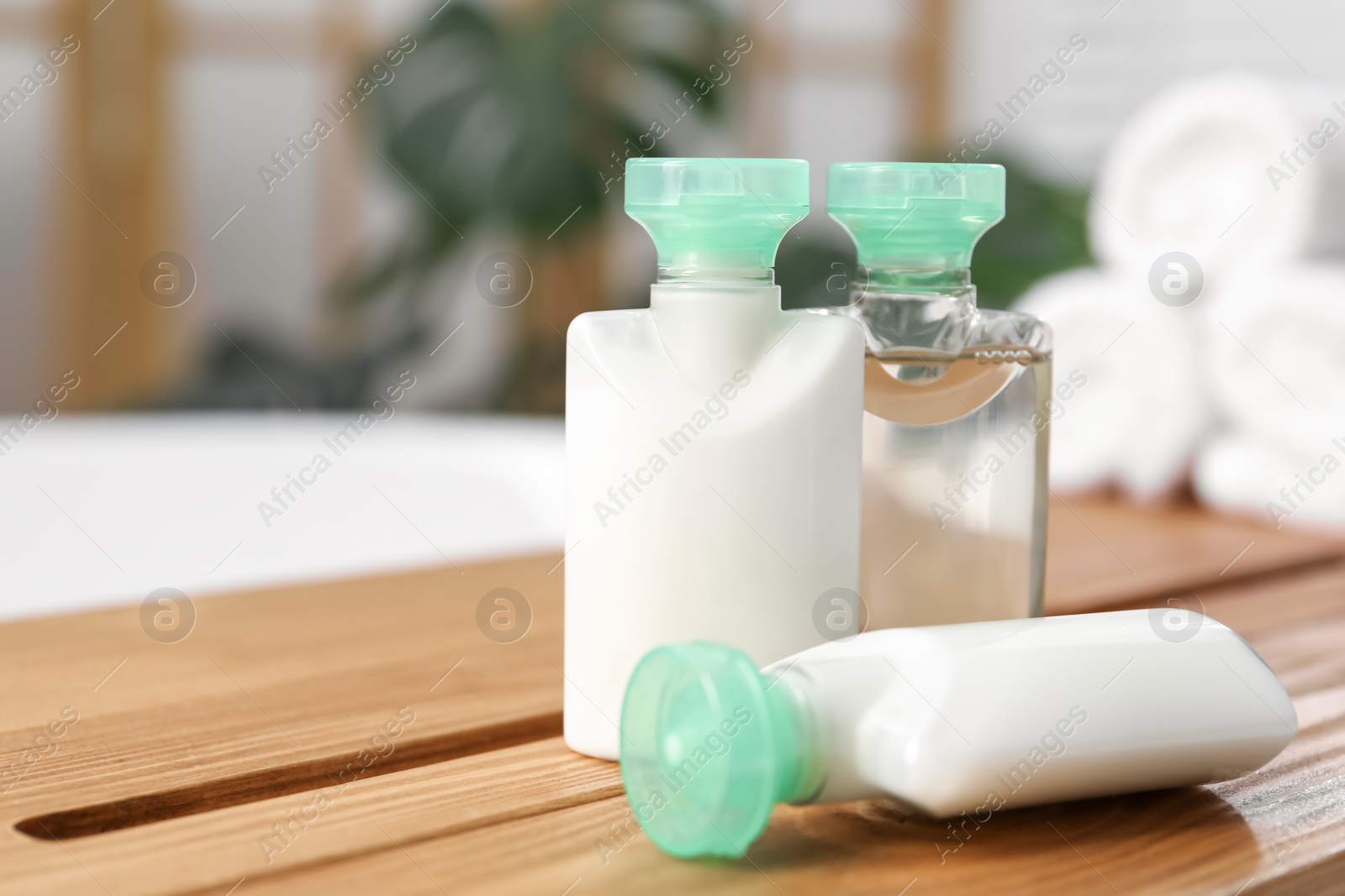 Photo of Wooden tray with mini bottles of cosmetic products on bath tub in bathroom, closeup. Space for text