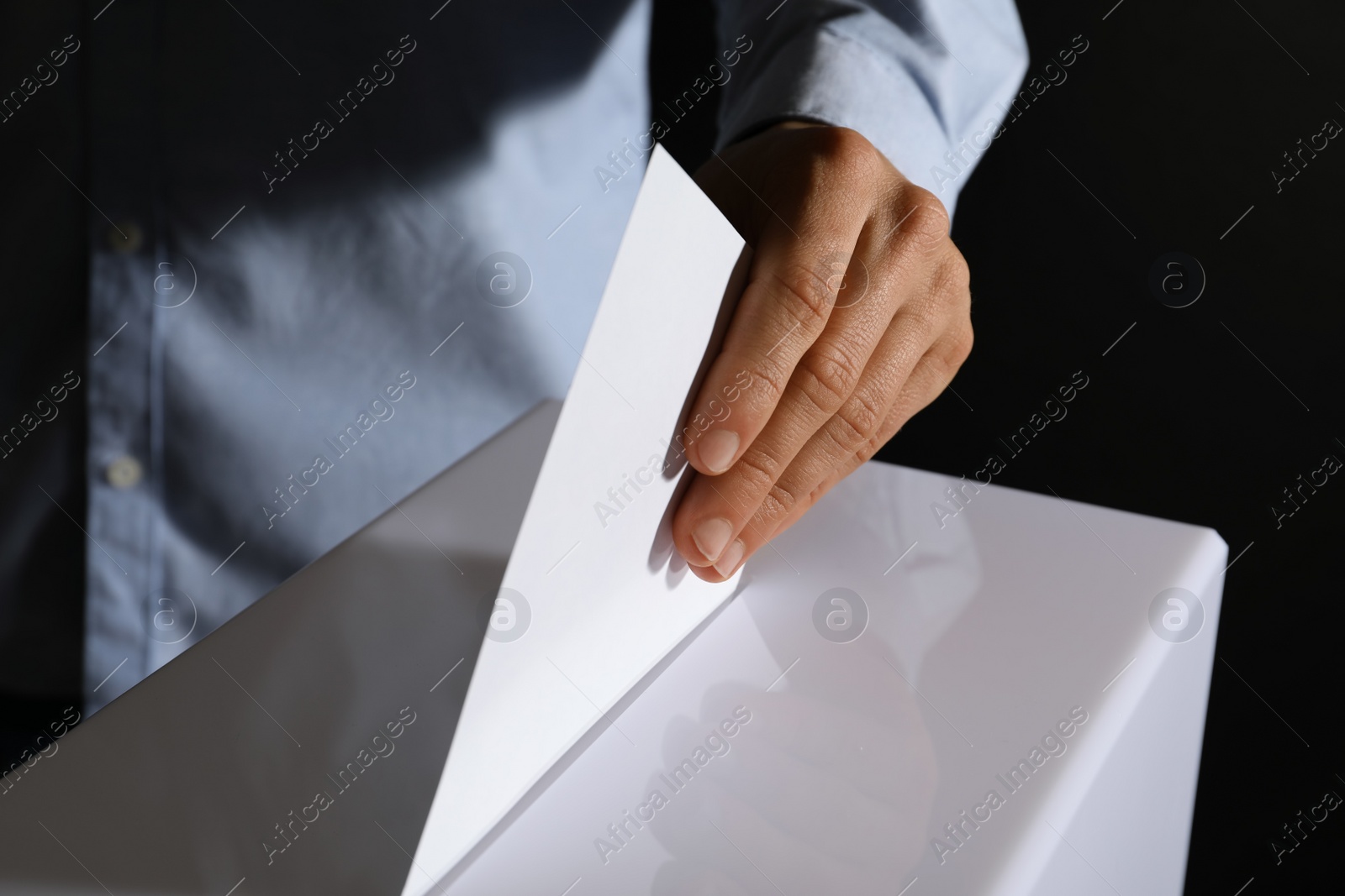 Photo of Man putting his vote into ballot box on black background, closeup