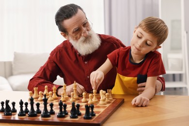 Senior man teaching his grandson to play chess at home