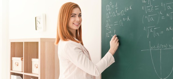 Image of Happy teacher writing on chalkboard in classroom. Banner design