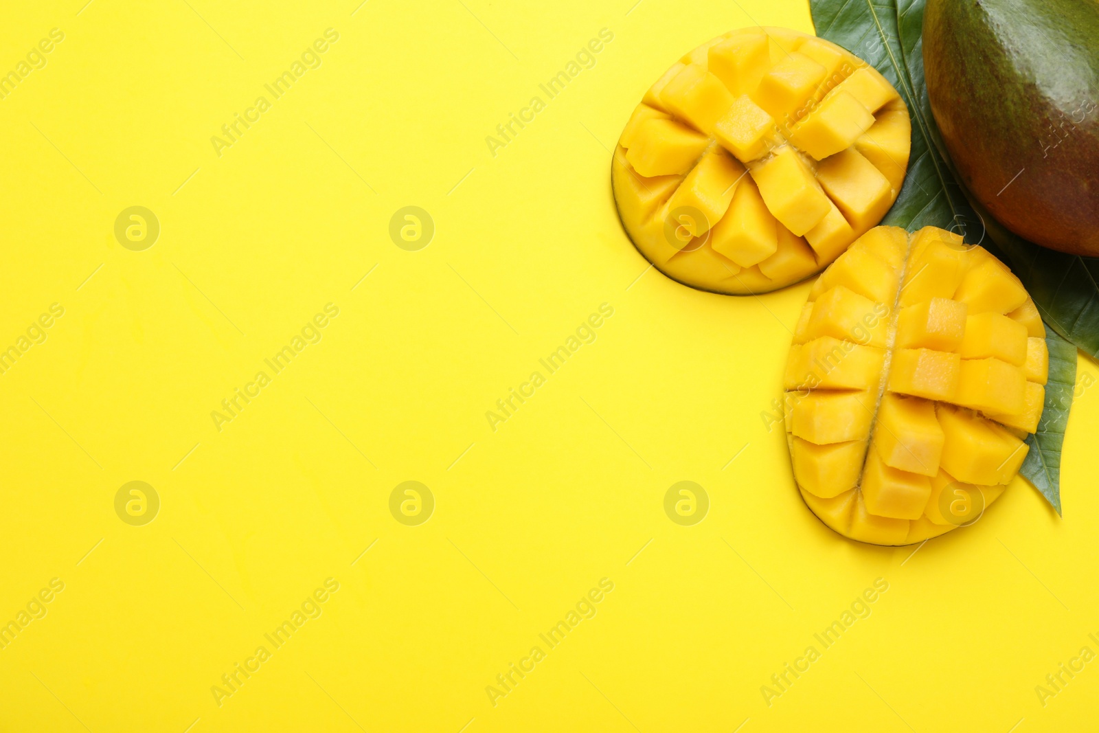 Photo of Cut fresh ripe mango and leaves on yellow background, flat lay. Space for text